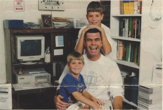 Michael Riley smiling with his two young sons in their home office, featured in a 1994 Military Lifestyle magazine article about ZilchWorks debt reduction software.